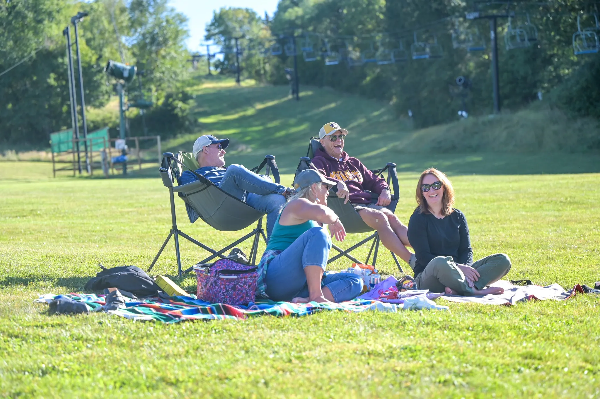 Friends and family sitting on picnic blanket in front of ski lift